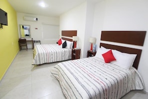 A hotel room with two beds, each with a striped bedspread and red and white pillows. There is a desk with a chair, a mirror, and a lamp. - Casa de la iaia Hotel (Orizaba)
