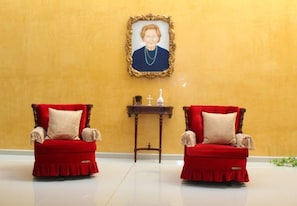 Two red armchairs with ruffled skirts and beige cushions, positioned in front of a wooden side table with a cross and a bottle. - Casa de la iaia Hotel (Orizaba)