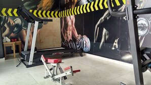 Une salle de sport équipée d’un tapis de course, d’un banc de musculation et d’une fresque murale représentant une figure musclée soulevant des poids.