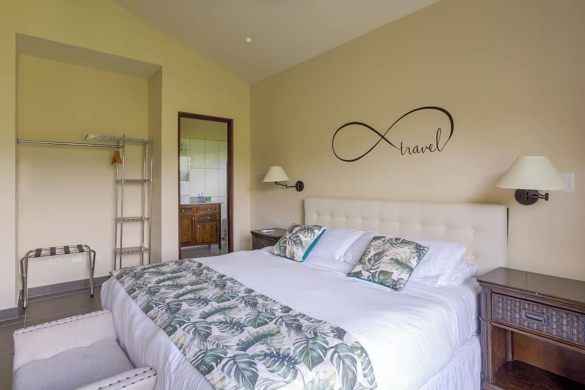 A hotel room with a bed, a wardrobe, a bathroom visible through an open door, and a wall with a 'travel' sign.