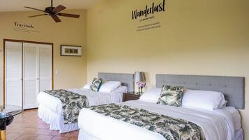 A hotel room with two beds, a ceiling fan, a wall with 'Wanderlust' and 'Travitude' definitions, and a framed picture on the wall.