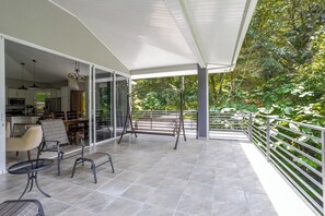A covered patio with a dining area, a kitchen visible through glass doors, and a view of a lush garden. - Coffee Estate Inn (Jaramillo)