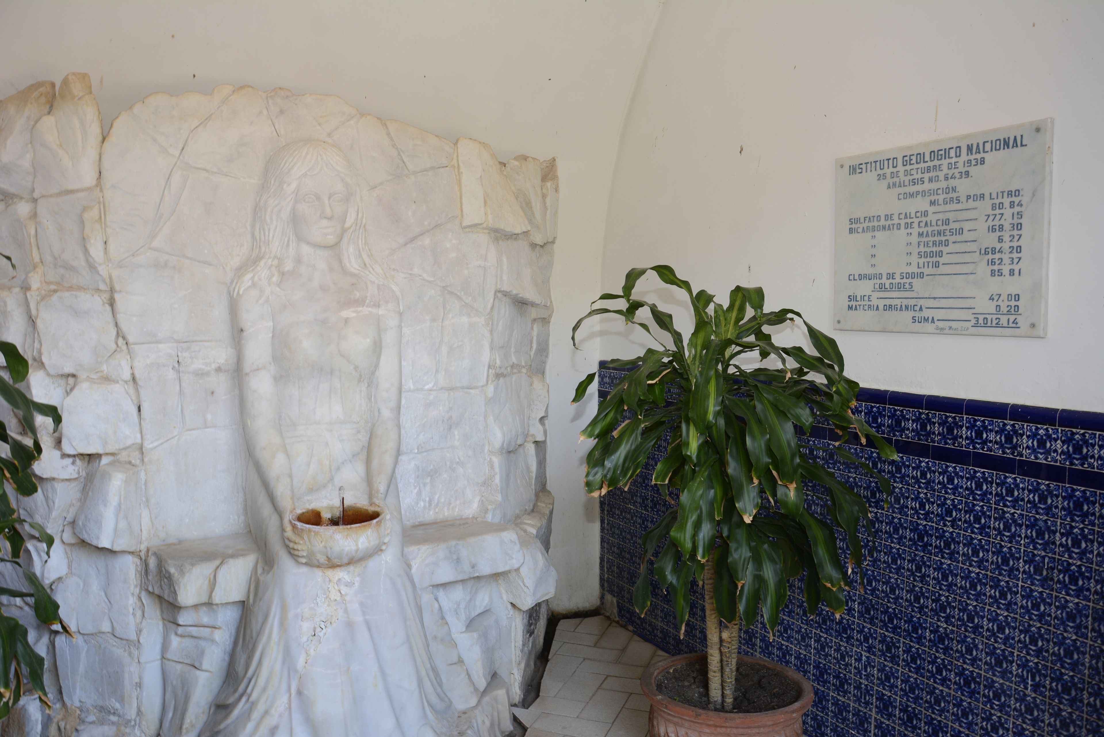A stone sculpture of a woman holding a bowl, a potted plant, and a geological composition chart on the wall.
