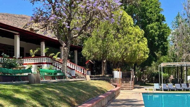 A pool area with a stone pathway, lounge chairs, and a building with a red roof and white columns. - Lourdes Hotel Campestre (Santa Maria del Rio)