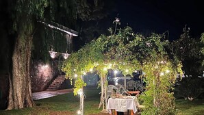 An outdoor dining area with a table set under a canopy of lights, surrounded by greenery. - Lourdes Hotel Campestre (Santa Maria del Rio)