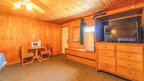 A wooden room with a ceiling fan, a television on a wooden cabinet, a microwave, and two chairs. - Green Acre Motel by OYO Near Rush County Airport (La Crosse)