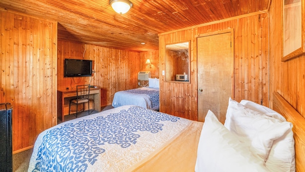 A wooden cabin room with two beds, a desk, a television, and a mirror. - Green Acre Motel by OYO Near Rush County Airport (La Crosse)
