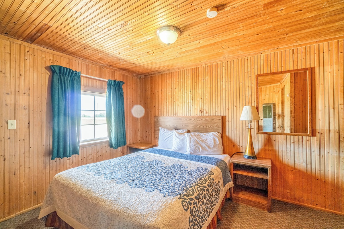 Habitación con paneles de madera, una cama, una mesita de noche, una lámpara y un espejo.