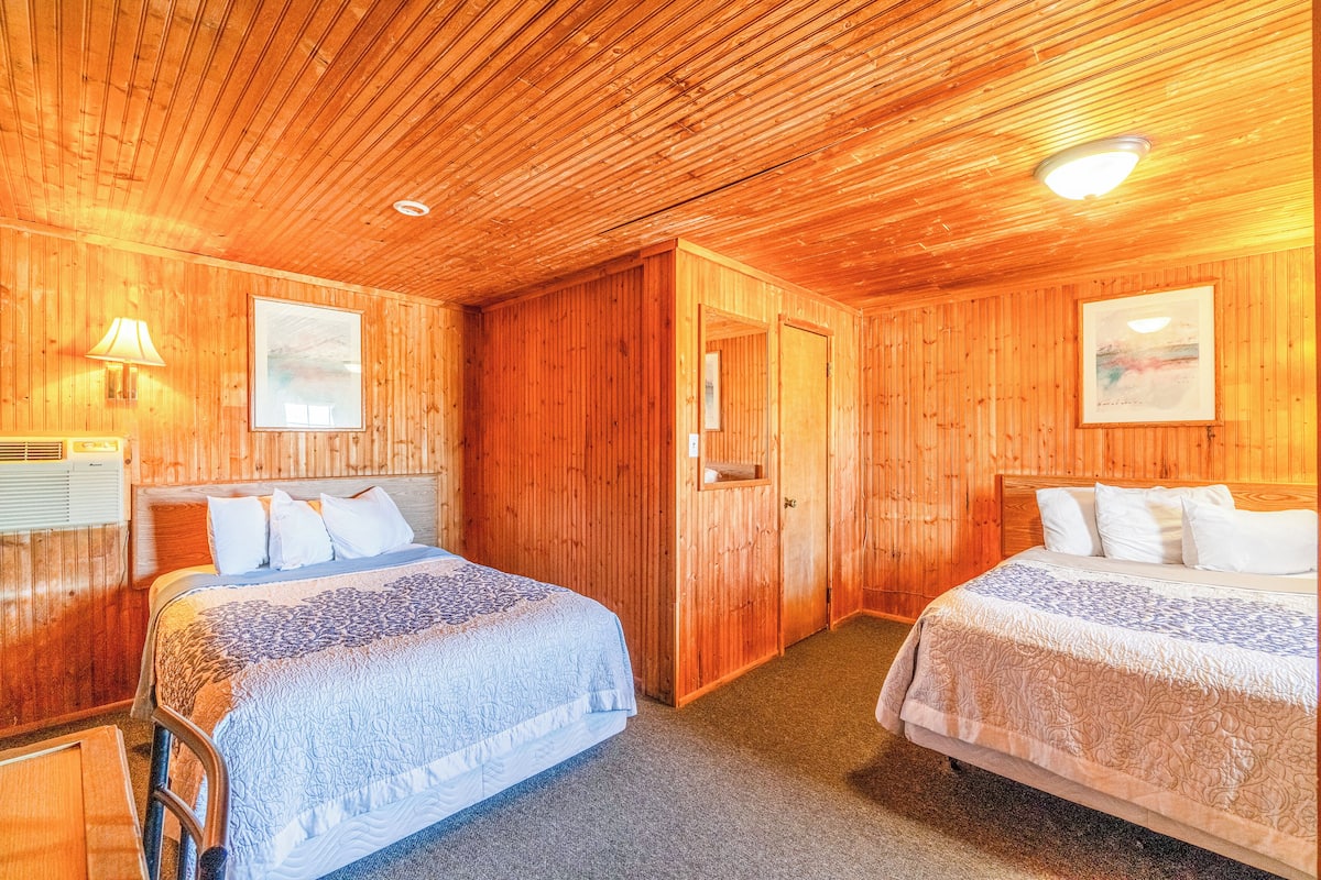 Una habitación con paneles de madera, dos camas, una puerta y un cuadro en la pared.