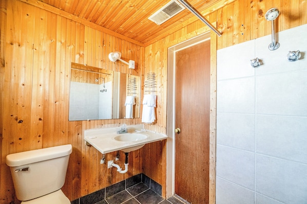 A wooden-paneled bathroom with a white sink, a toilet, and a shower area. - Green Acre Motel by OYO Near Rush County Airport (La Crosse)