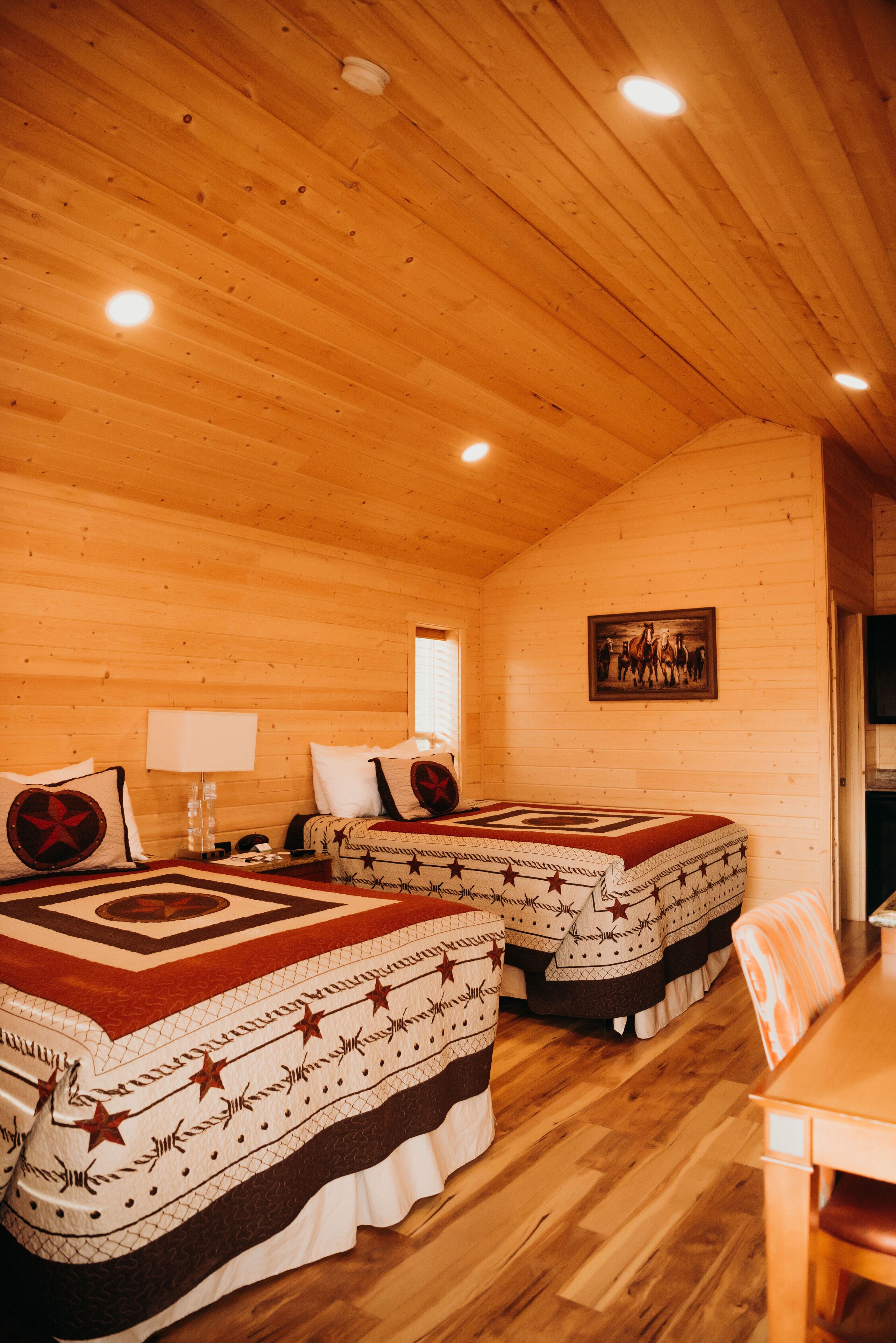 Una habitación tipo cabaña con dos camas, paredes de madera e iluminación empotrada en el techo.
