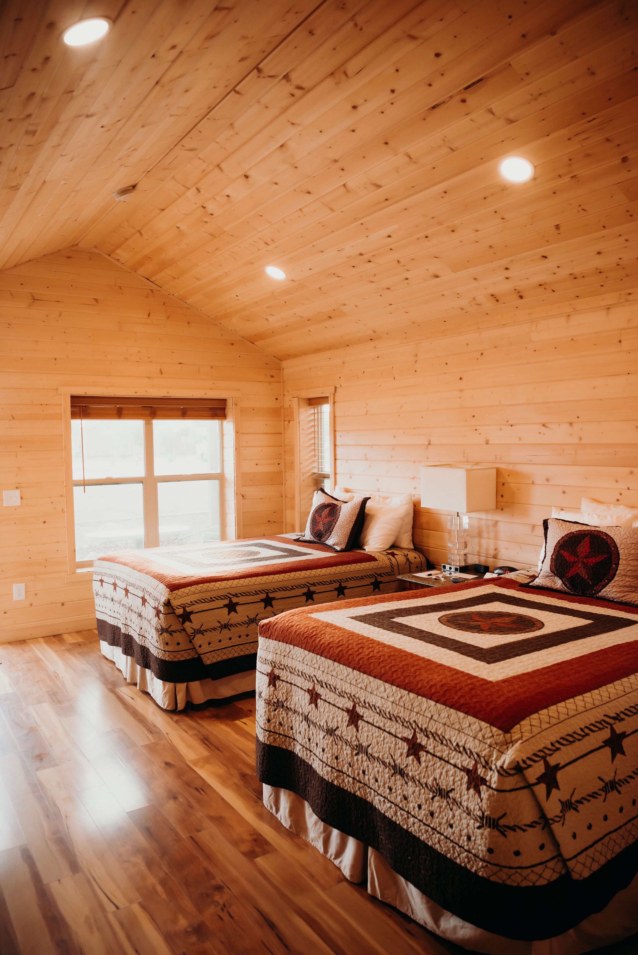 Una cabaña con dos camas, pisos de madera y un ventanal grande.