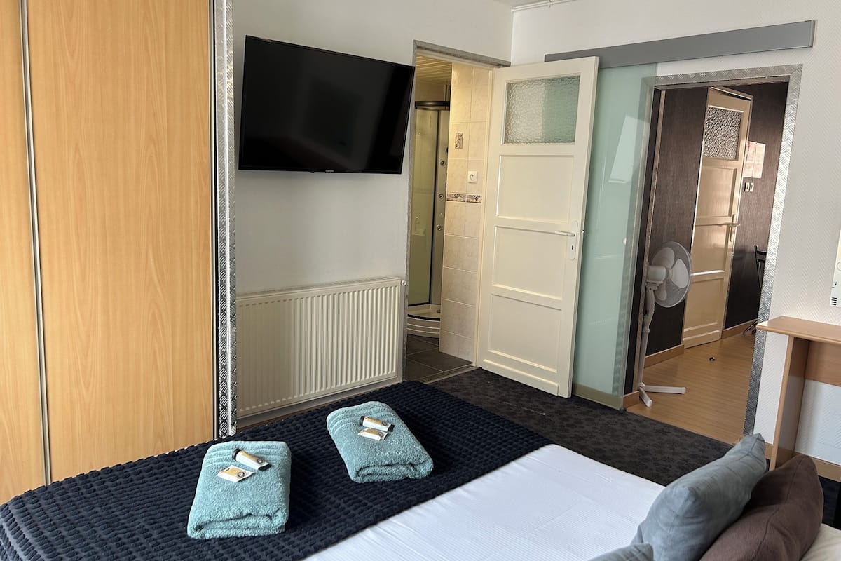 A hotel room with a bed, two towels, a TV, and a door leading to a bathroom.
