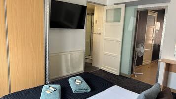 A hotel room with a bed, two towels, a TV, and a door leading to a bathroom.