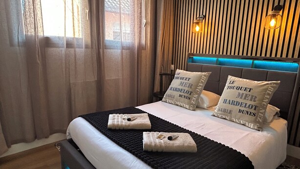 A hotel room with a bed, two pillows with text, a headboard with blue lighting, and curtains. - Résidence Chez Gino (Etaples)