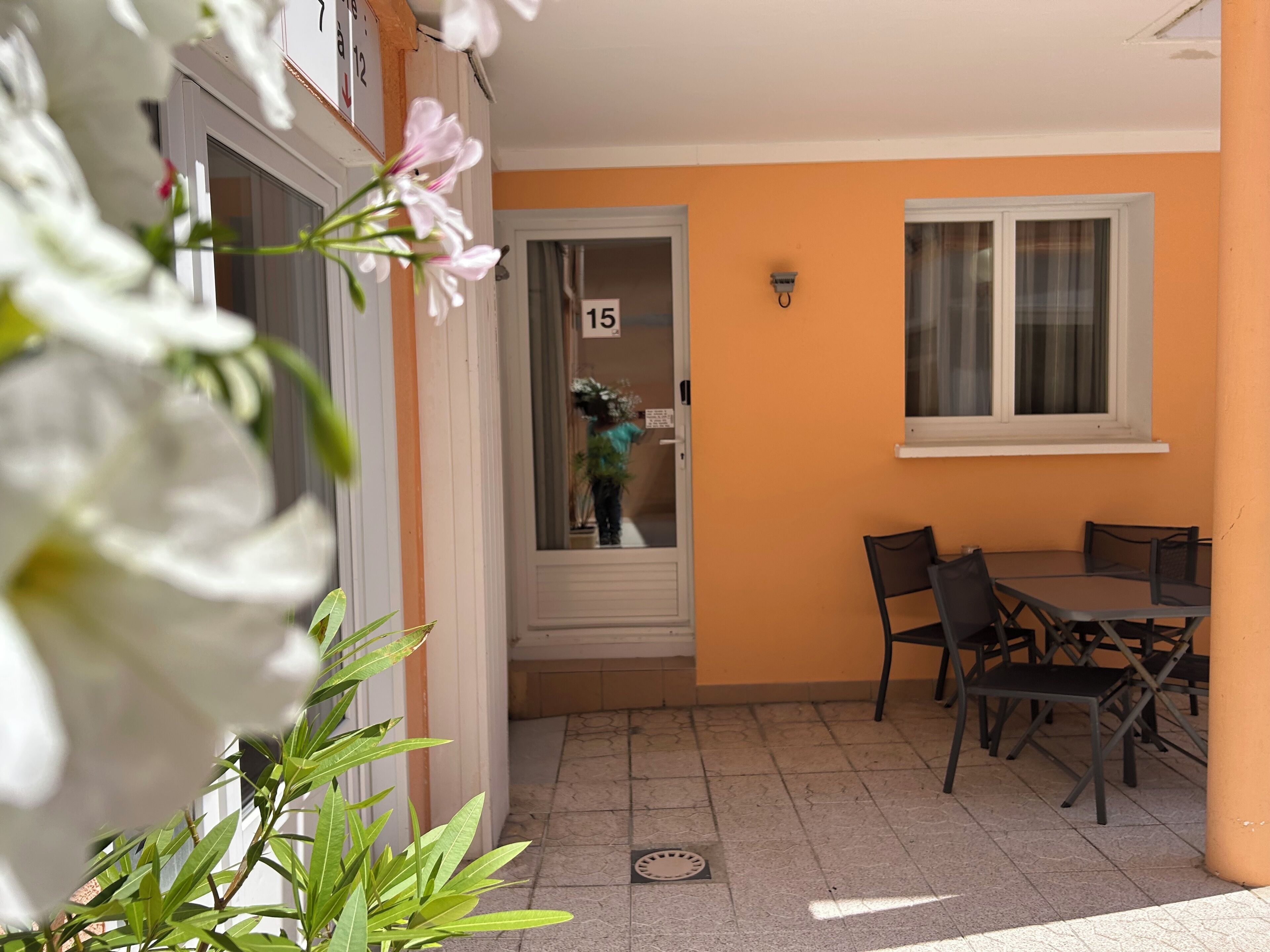 A balcony with a table and chairs, a door with a number sign, and a window.