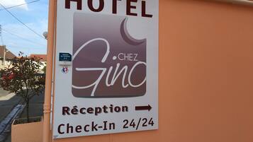 A hotel sign with "HOTEL" at the top, "RÉCEPTION" and "Check-In 24/24" below, and an arrow pointing right.