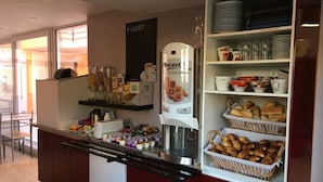 A breakfast bar with a coffee machine, shelves with plates and cups, and baskets of pastries. - Résidence Chez Gino (Etaples)