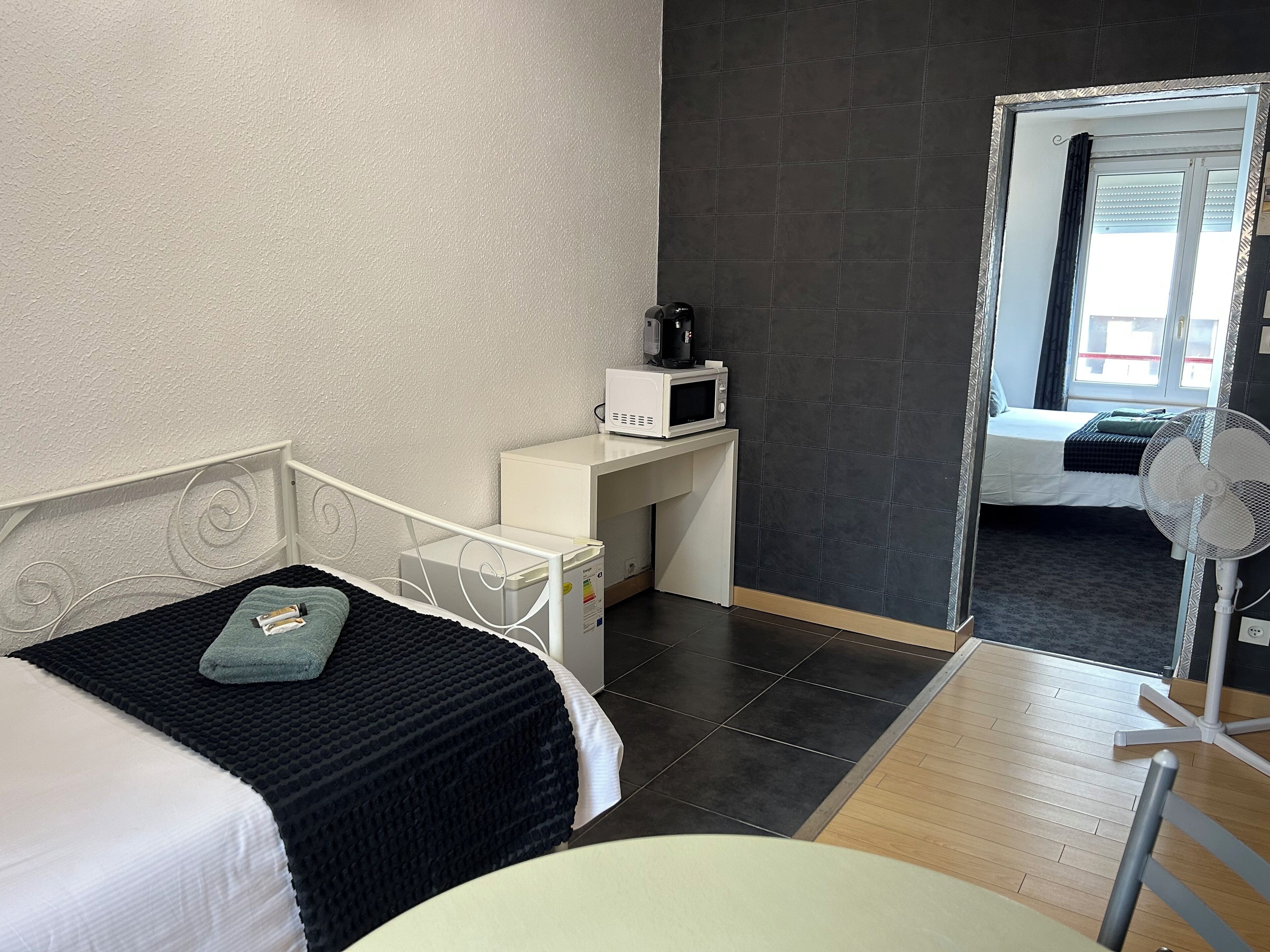 Une chambre avec un lit, un bureau doté d’un micro-ondes, un ventilateur et une vue sur une autre pièce.