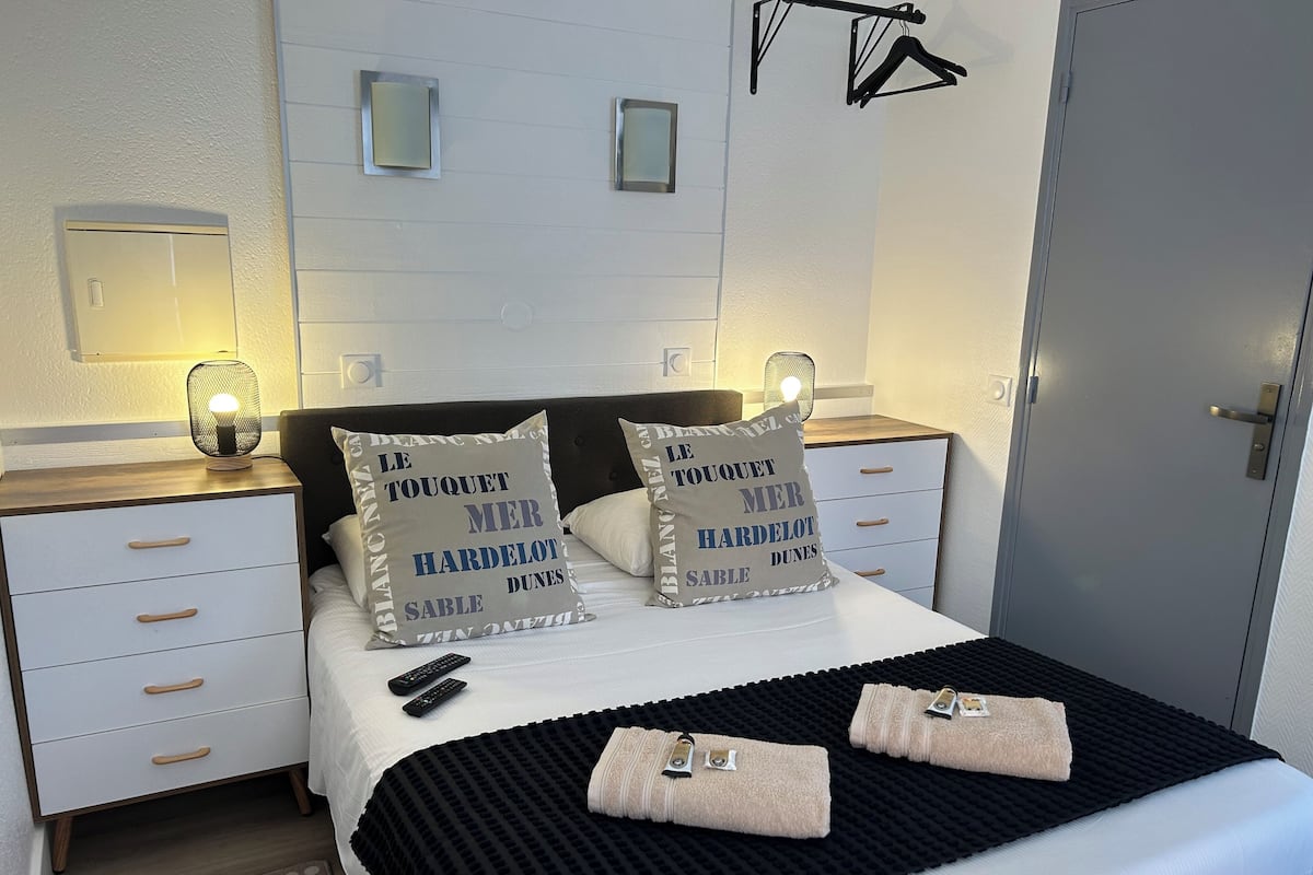 A neatly made bed with two pillows, a bedside table with a lamp, and a door to the right.