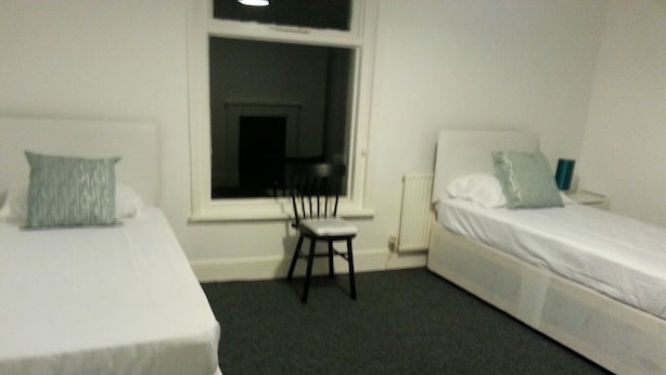 A small, sparsely furnished room with two single beds, a chair, and a window. - Icon Harwich Apartment (Harwich)