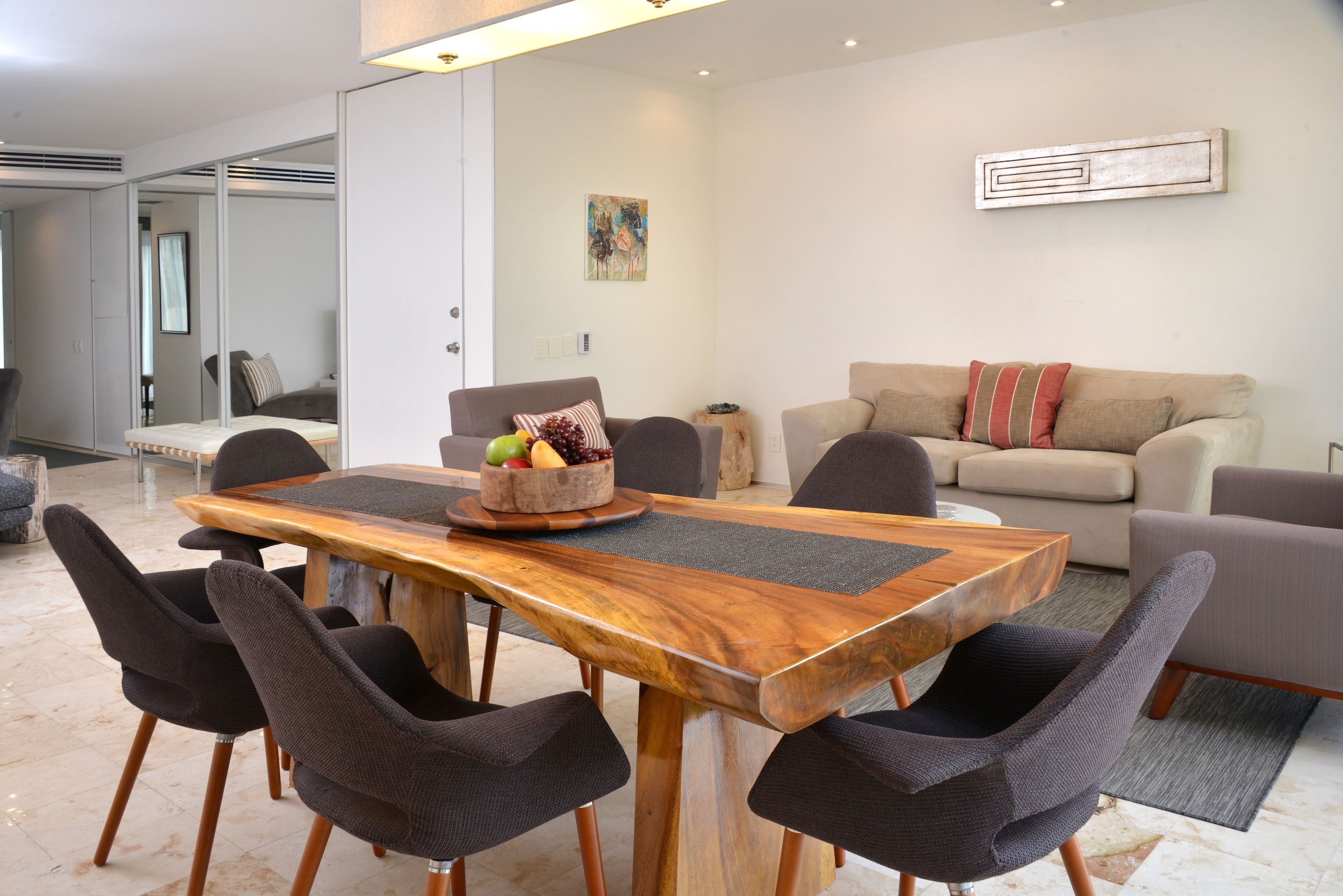 A modern dining area with a wooden table and dark chairs, a beige sofa, and a small side table with a fruit bowl.