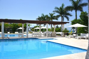 A clear blue pool with white lounge chairs and umbrellas under a pergola. - Magia Beachside Condo (Playa del Carmen)