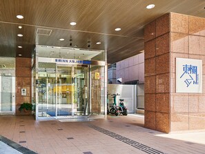 Una entrada de hotel con diseño moderno, que incluye un acceso por puerta de vidrio, un letrero con caracteres japoneses y piso de baldosas.
