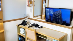 A hotel room with a desk, a telephone, a computer monitor, a mirror, and a small refrigerator.