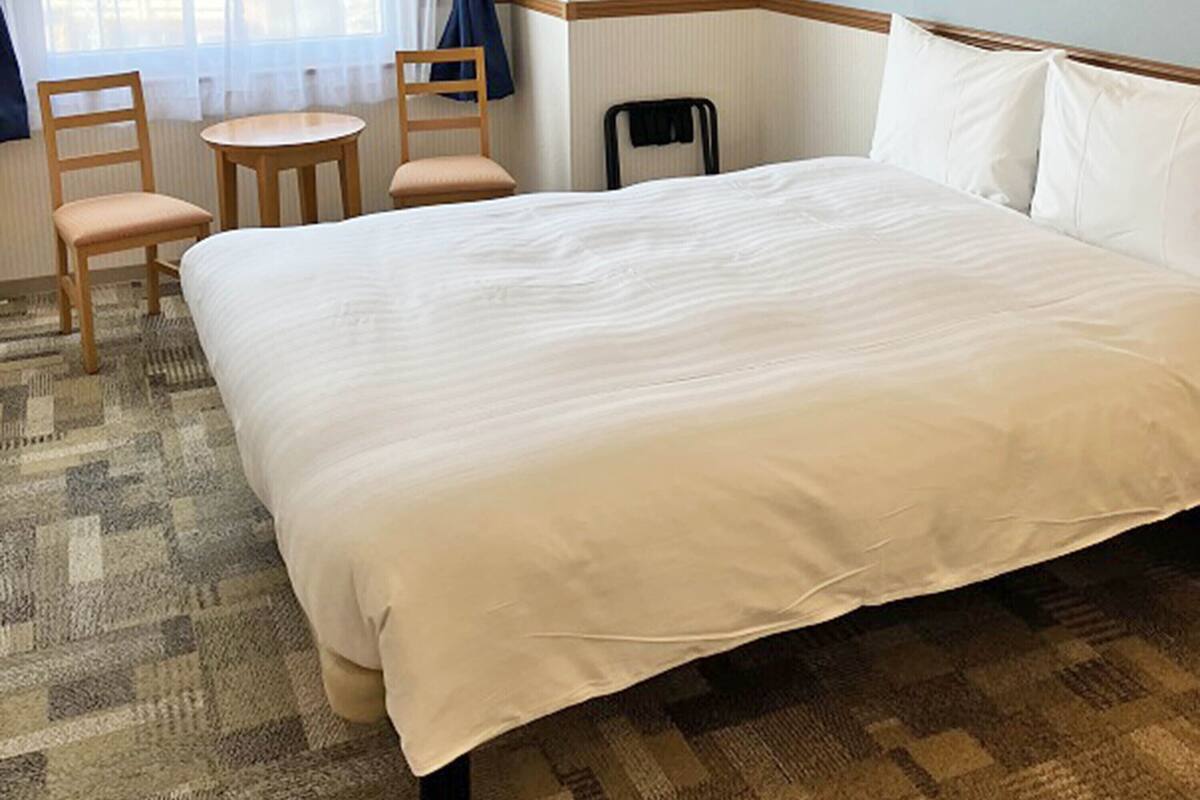 A hotel room with a large bed, a small round table, two chairs, and a window with curtains.