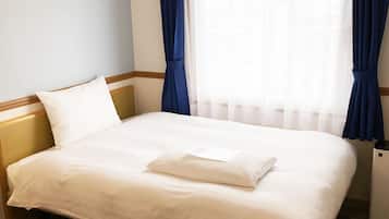 Een net opgemaakt bed met witte lakens in een hotelkamer, met een houten hoofdeinde, een klein nachtkastje en blauwe gordijnen.