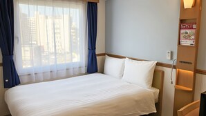 A hotel room with a large bed, a window with curtains, a bedside table, and a wall-mounted light fixture.