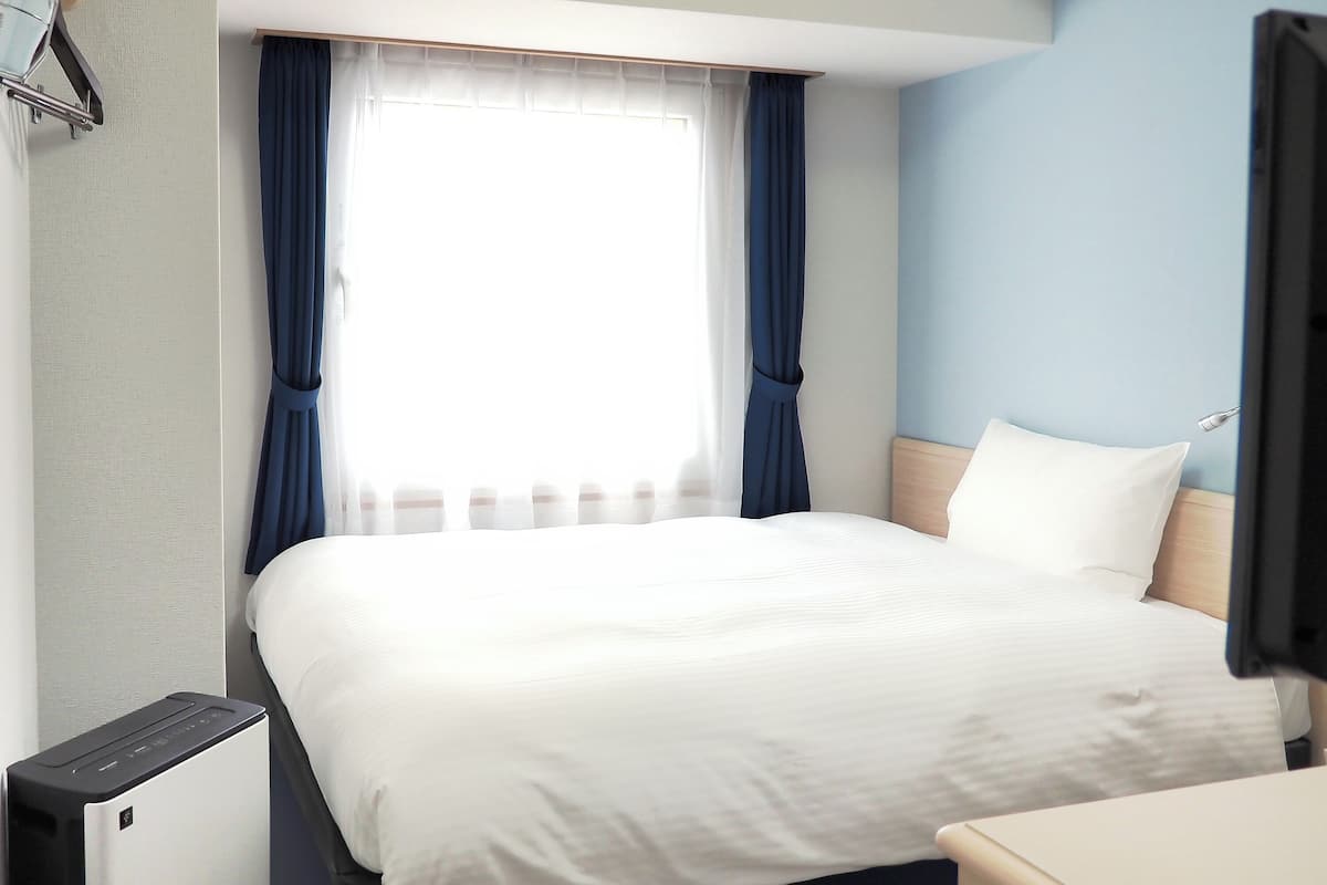 A hotel room with a bed, a desk, a chair, a TV, and a window with curtains.