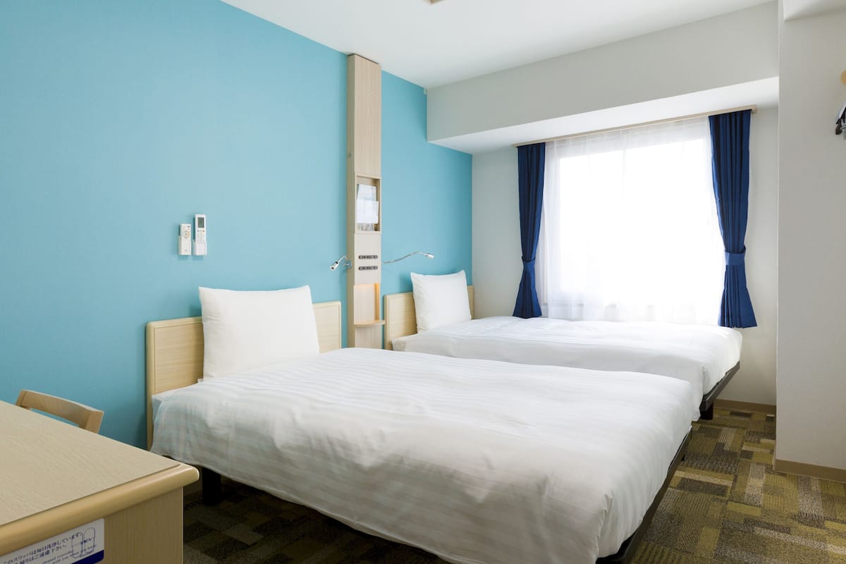 Ein Hotelzimmer mit zwei Betten, einem Schreibtisch und einem Fenster mit Vorhängen.