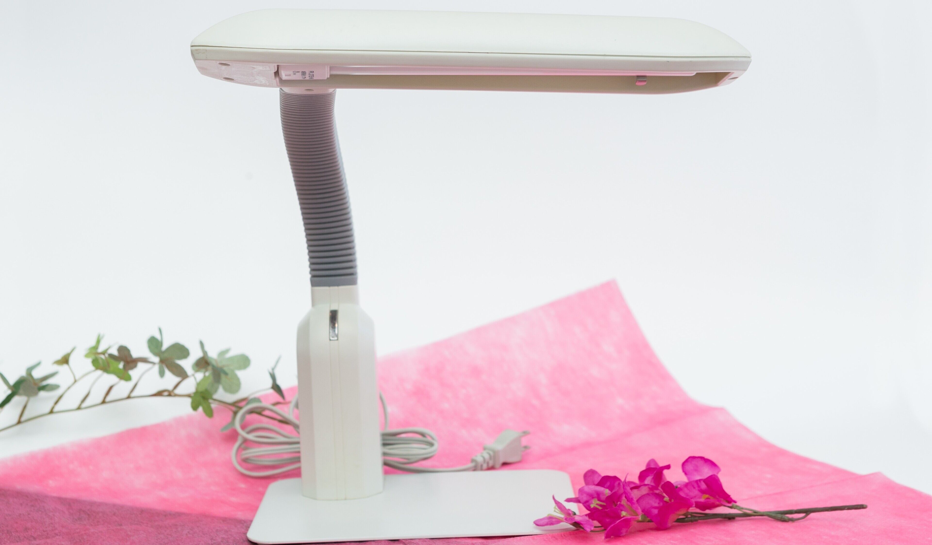 A white massage table with a textured handle, placed on a pink surface with a flower and a plant.