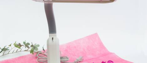 A white massage table with a textured handle, placed on a pink surface with a flower and a plant.