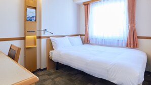 Habitación de hotel con cama, escritorio, silla, lámpara de pared y ventana con cortinas.