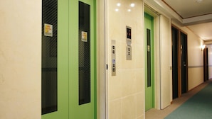 Un pasillo con puertas verdes, un ascensor y una alfombra con un logotipo.