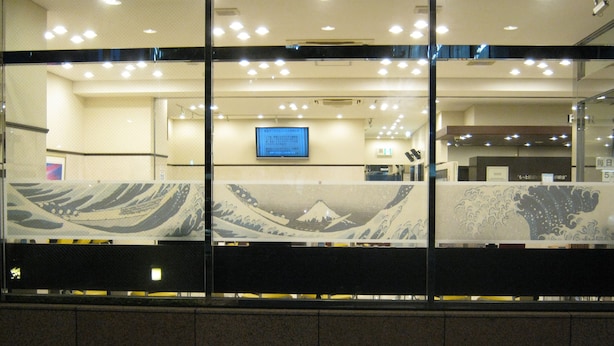 Un interior moderno con una gran pantalla digital, divisiones de vidrio con diseños ondulados y piso de baldosas.