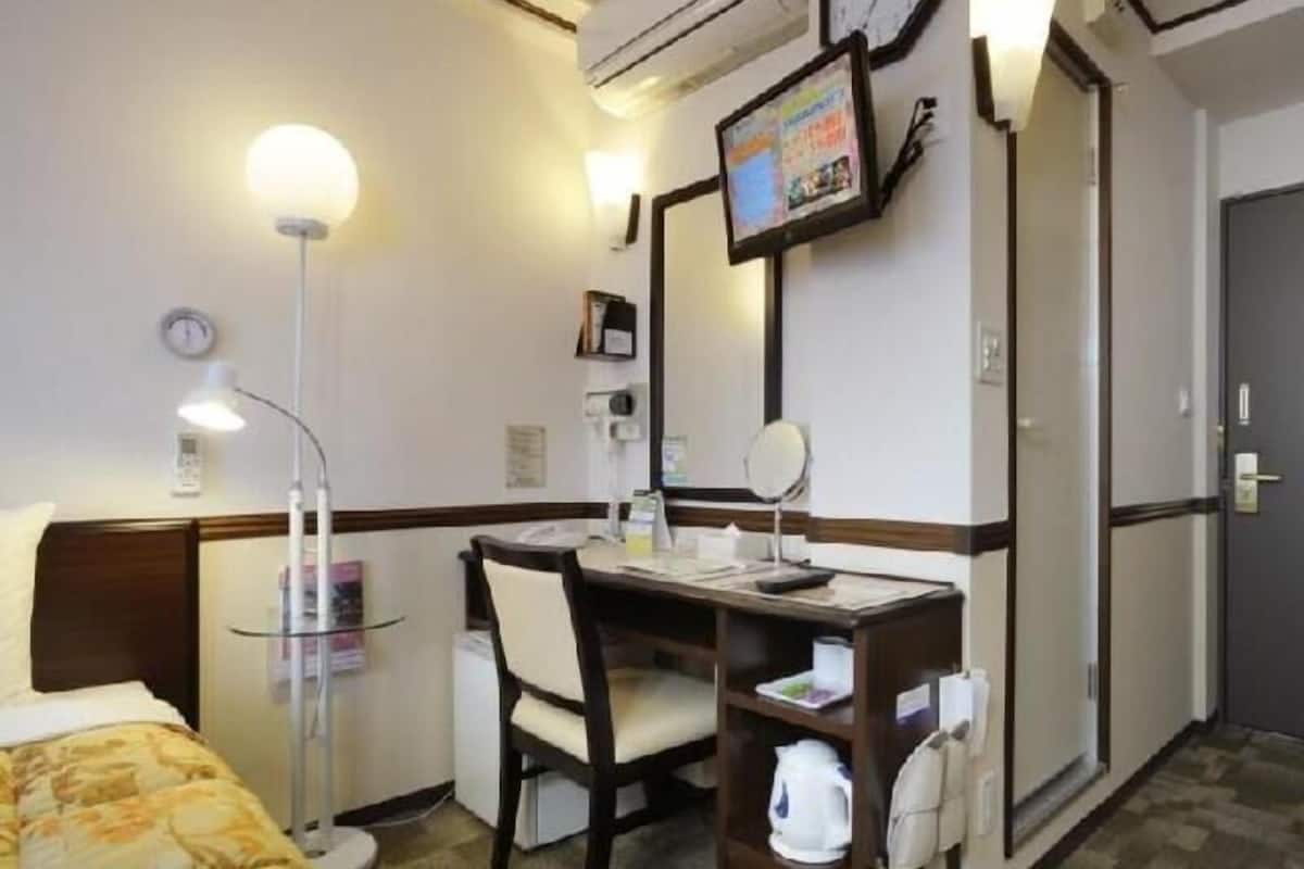 Una habitación de hotel con cama, escritorio, silla, lámpara de escritorio, reloj, equipo de aire acondicionado y televisor montado en la pared.