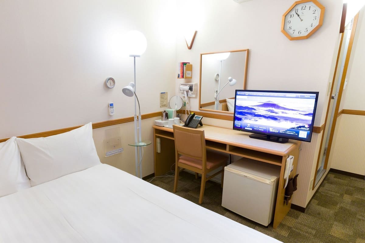 A hotel room with a bed, desk, chair, and a television displaying a landscape.