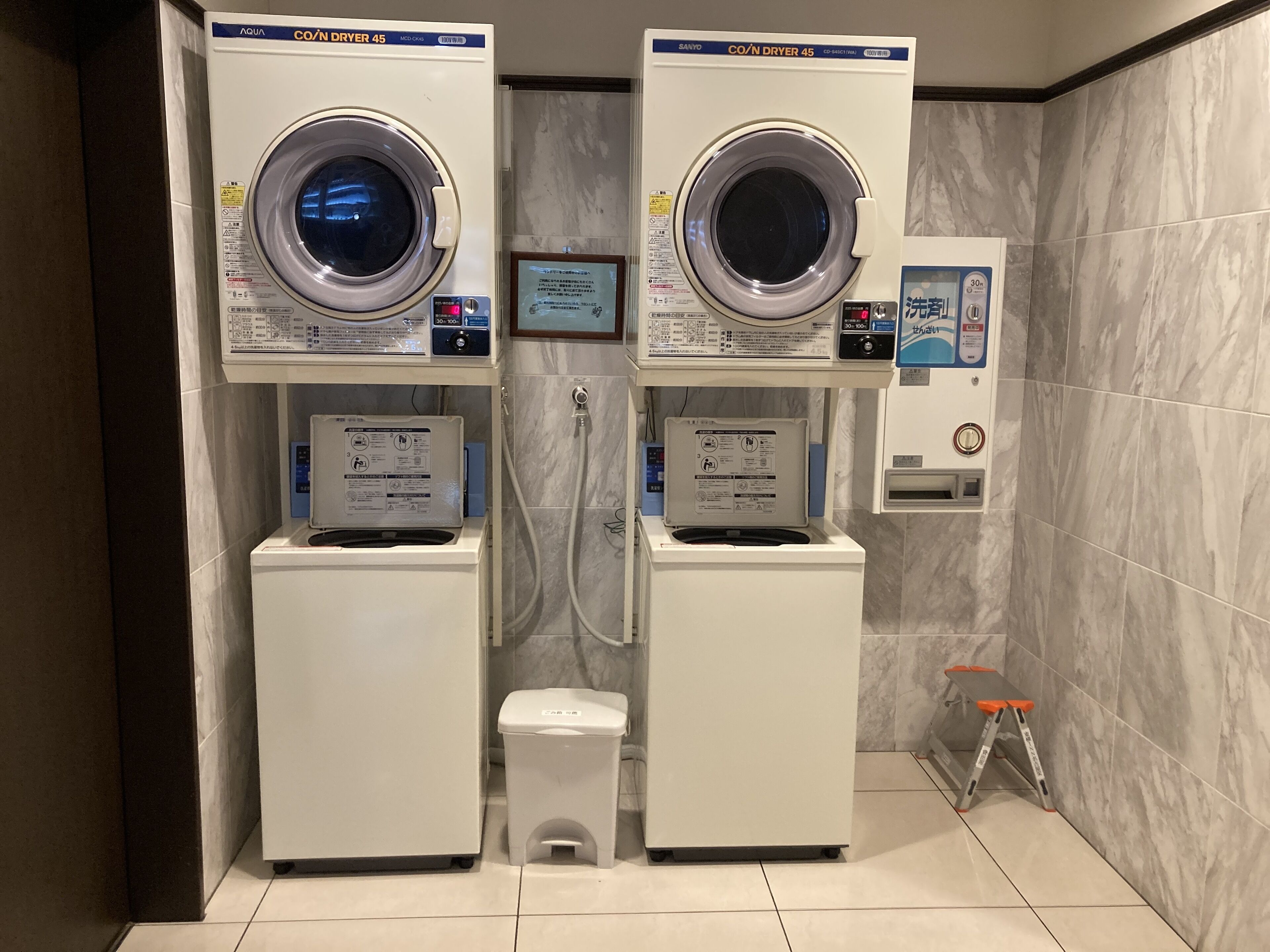 A laundry facility with two front-loading washers and dryers, a small stool, and a step ladder.