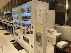 Una fila de máquinas expendedoras en el vestíbulo de un hotel, cada una con diferentes bebidas y aperitivos.