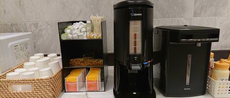 A coffee machine, tea dispensers, and a basket of disposable cups on a countertop.