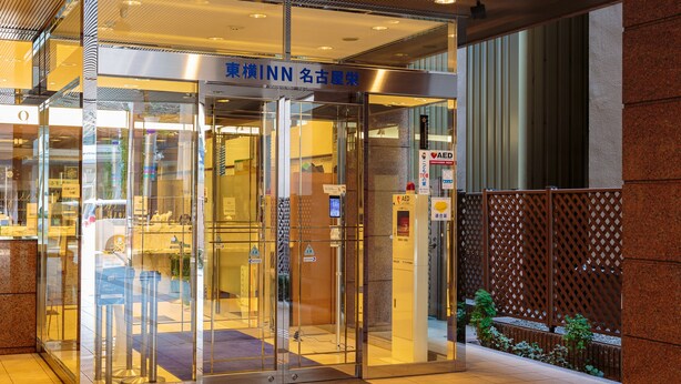 Entrada de hotel con puerta de cristal, un letrero que dice 'INN' y una estación de desfibrilador.