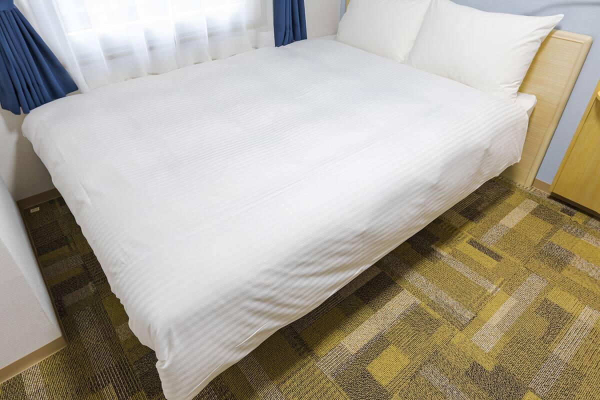 A large bed with white bedding, a wooden headboard, and a checkered carpet.