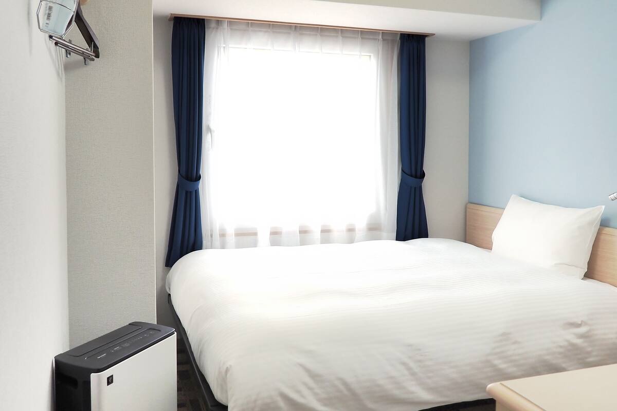 A hotel room with a bed, a desk, and a window with curtains.