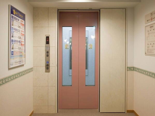 Un ascensor con pantalla digital y puerta rosa, flanqueado por paredes color beige con bordes estampados.