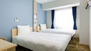 Hotellihuone, jossa on kaksi sänkyä, työpöytä, peili ja ikkuna, jossa on verhot.