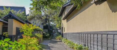 Un callejón tradicional japonés con un sendero adoquinado, rodeado de follaje y edificios tradicionales.